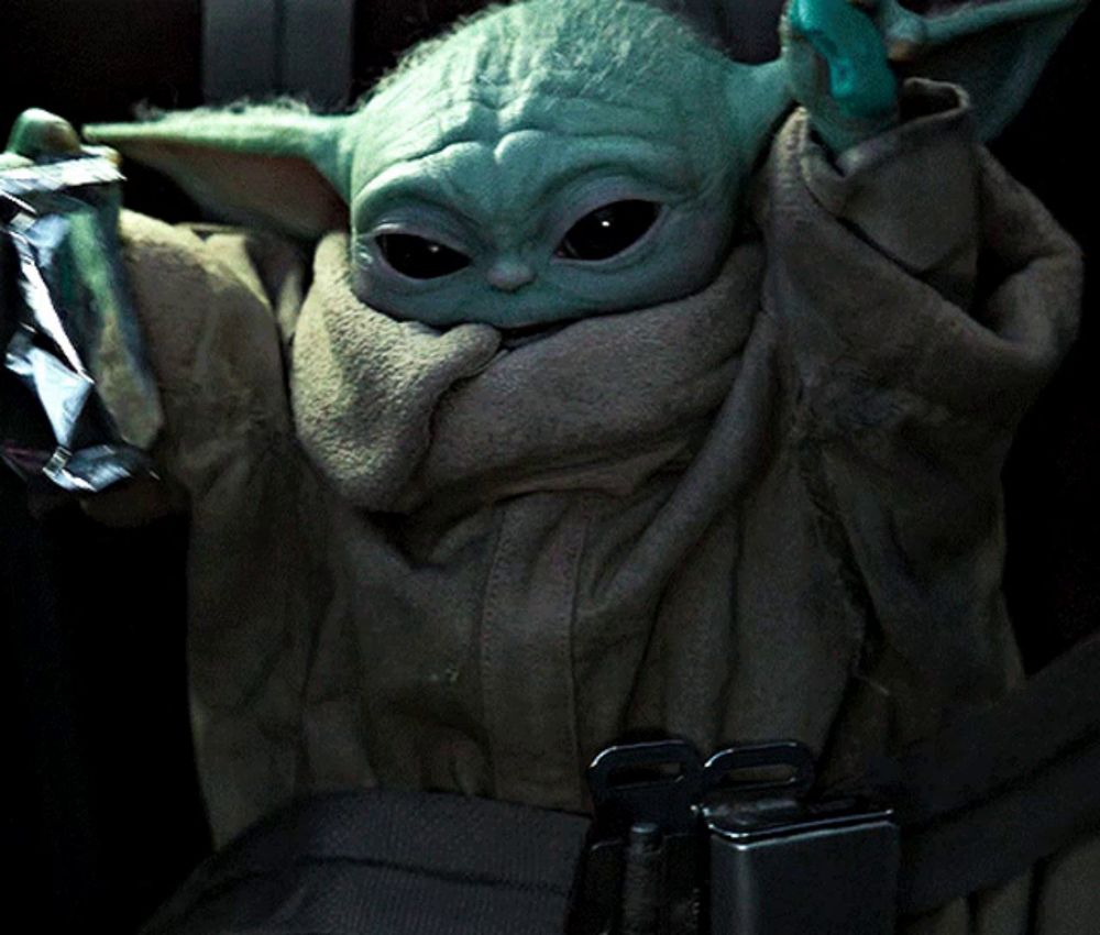 a baby yoda is sitting in a car seat holding a piece of aluminum foil