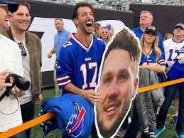 Former F1 driver Daniel Ricciardo standing on the sidelines wearing a Josh Allen jersey, holding a fat head of his lover Josh Allen