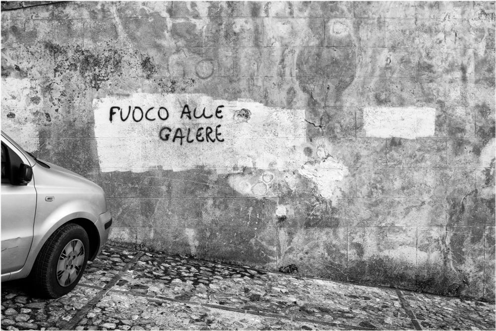 La scritta "Fuoco alle galere" su un muro a Spoleto, provincia di Perugia, Italia. Foto in bianconero, 2021.