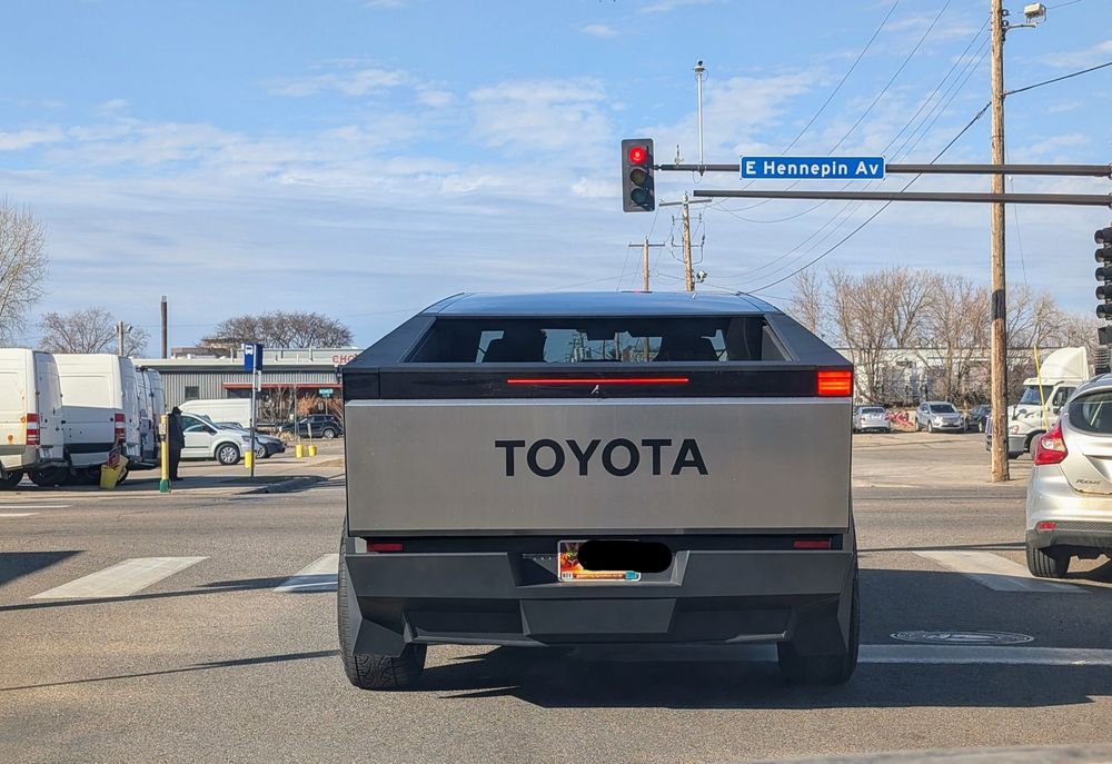 A gray cyber truck with a large Toyota logo on the tailgate waits at a red light on East Hennepin Avenue