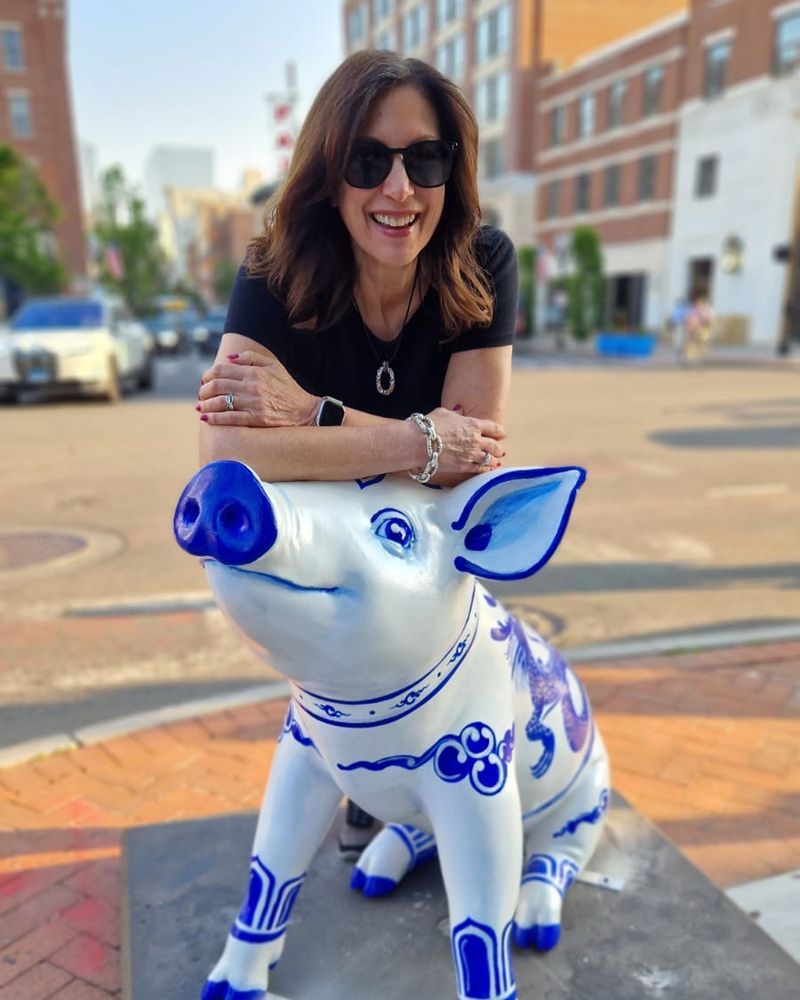The author is leaning on a fiberglass pig sculpture on a street in Stamford. The pig is seated and the outside of its body is covered in Chinese symbols to replicate antique porcelain.