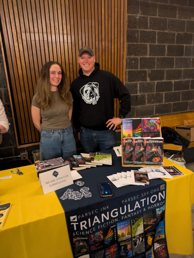Jess Carver and Greg Clumpner standing behind a table that features Triangulation books.