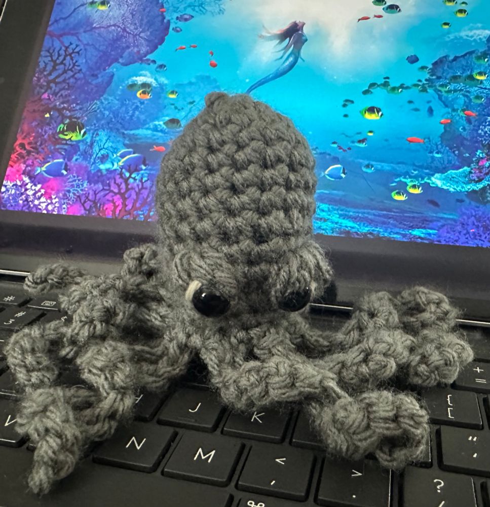 Gray crocheted octopus with angry expression.