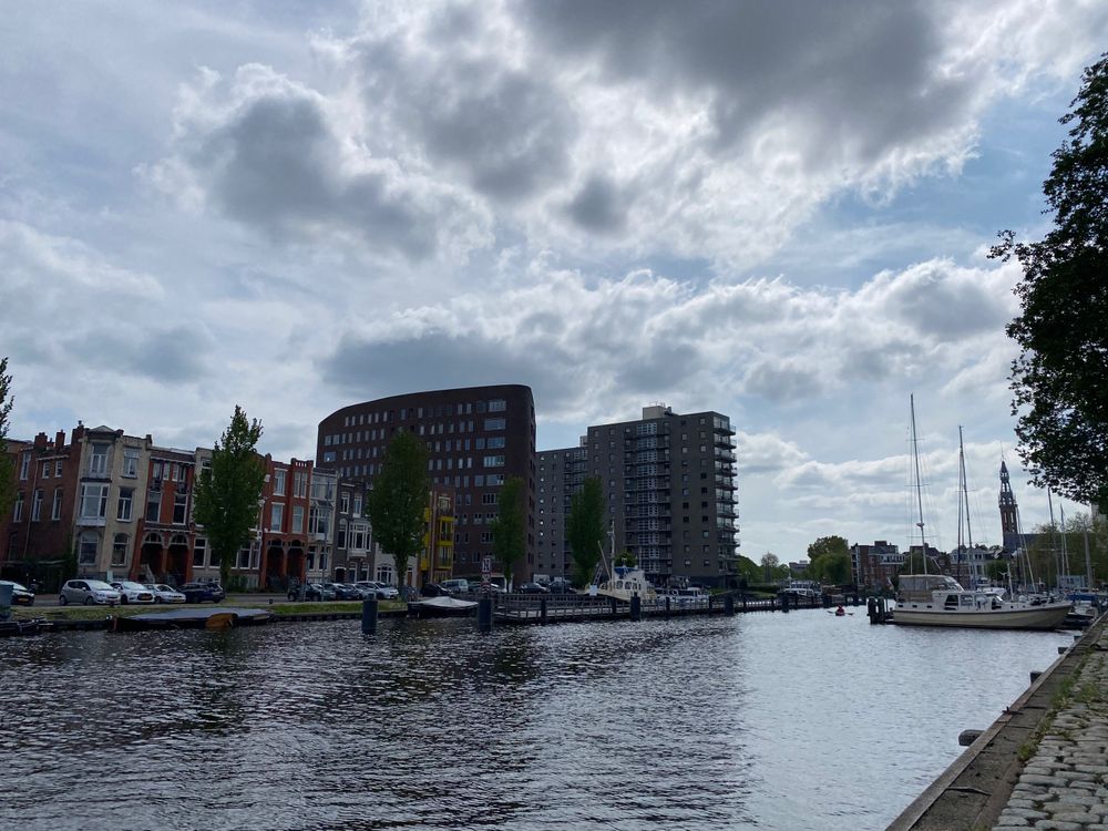 Photo is of houses and boats along a canal with blue sky trying to break through some dramatic grey clouds