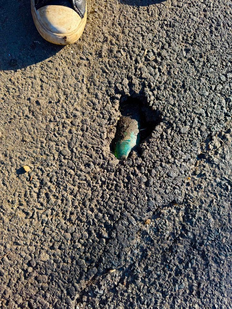 Green glass bottle imbedded in road surface tarmac 