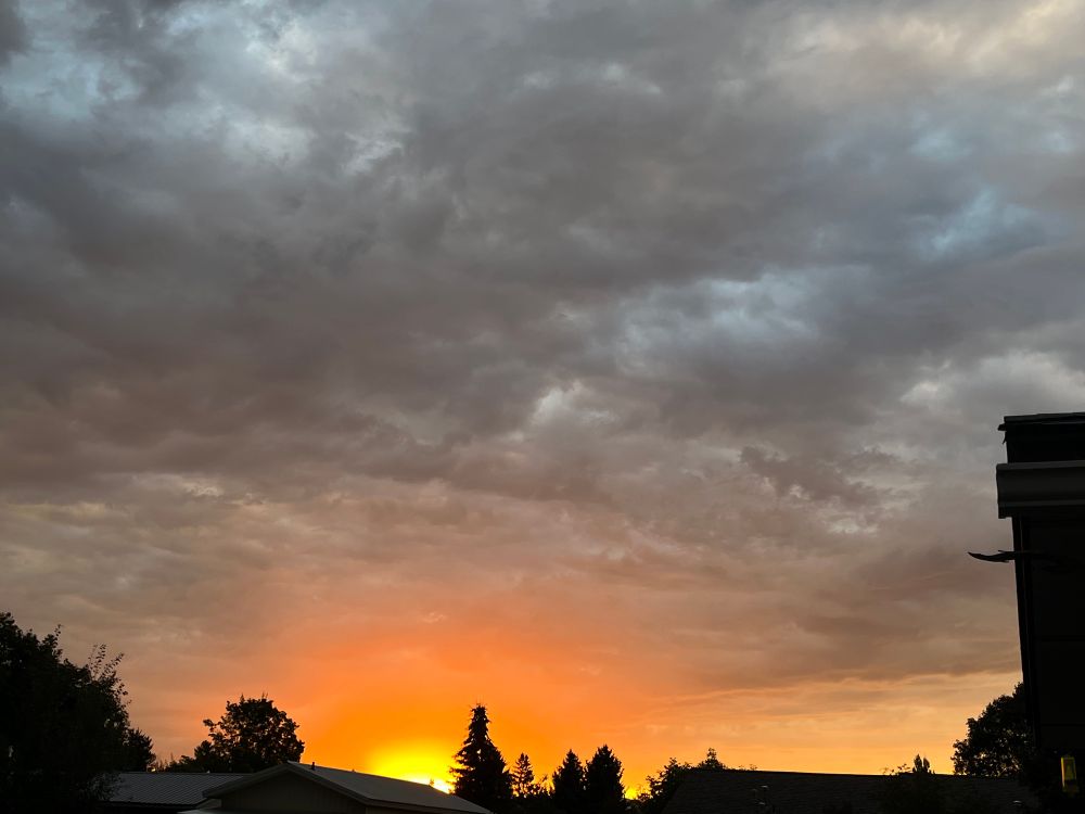 The bright yellow glare of the sun as it rises produces an orange glow underneath dark gray storm clouds. 
