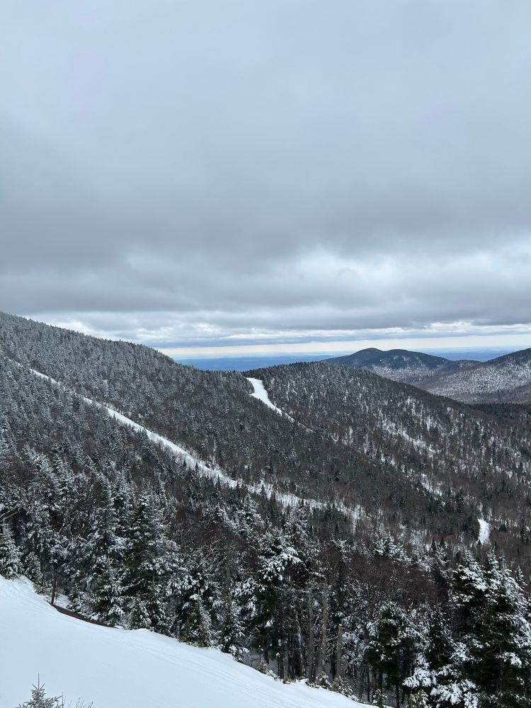 Mountain covered in trees with snow, two ski slopes visible. Gray skies. Jay Peak, Vermont.