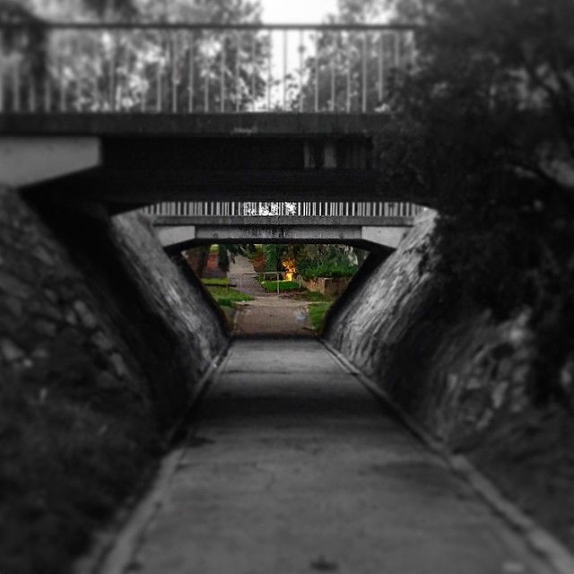 A black and white image of an underpass with the view at the end in colour. 