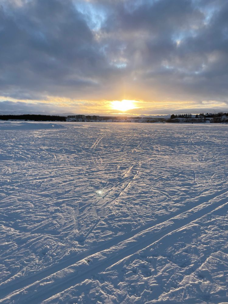 view of a frozen lake with skiing tracks and the winter sun
