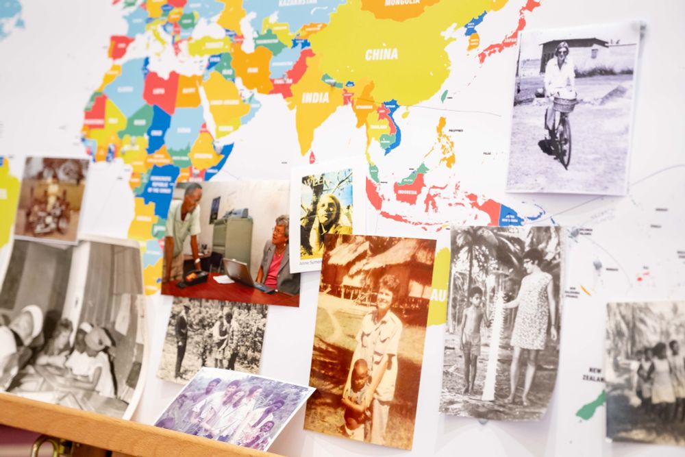 A pin-board of a colourful world map has photographs attached to it showing different VSO volunteers in different locations across the globe.