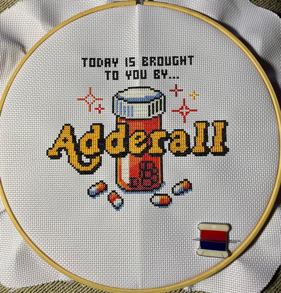 Cross stitch that says “Today is brought to you by… Adderall” with a pill bottle in the background and scattered pills along the bottom