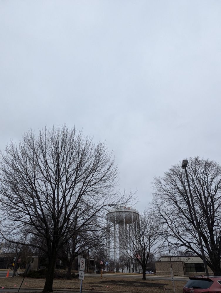 A water tower and trees outlined against a cloudy sky.
