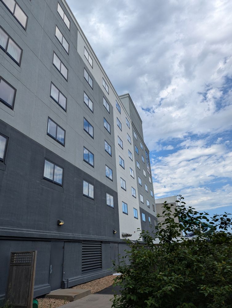 The back side of a hotel, windows reflecting a blue, clouded sky.