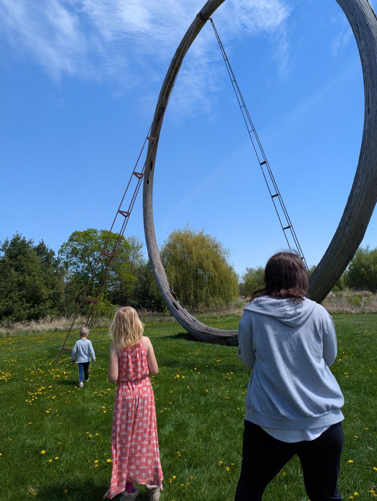 Three people in front of a sculpture of a large circle.