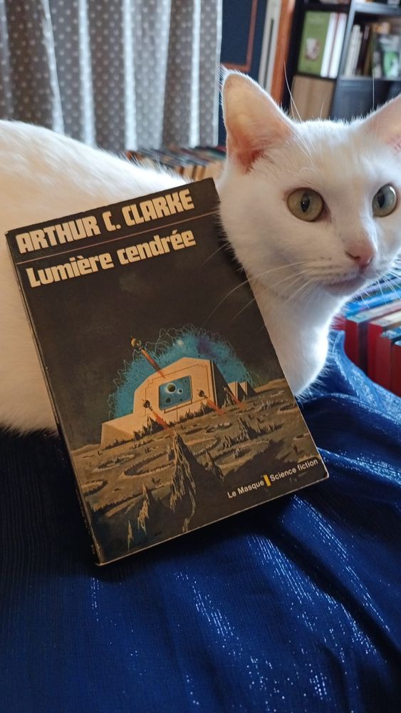 L'ouvrage Lumière cendrée d'Arthur C. Clarke posé sur un chat, posé sur un tissu, posé sur un pouf.
