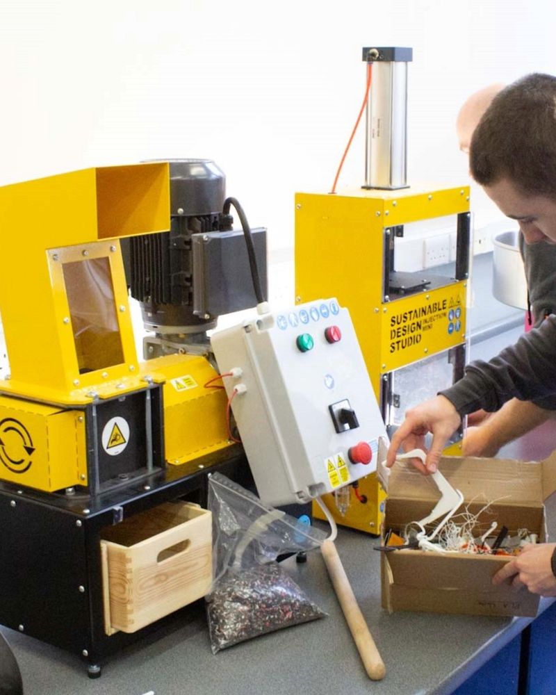 male sifts through a box of items beside a yellow machine which says sustainable design studio