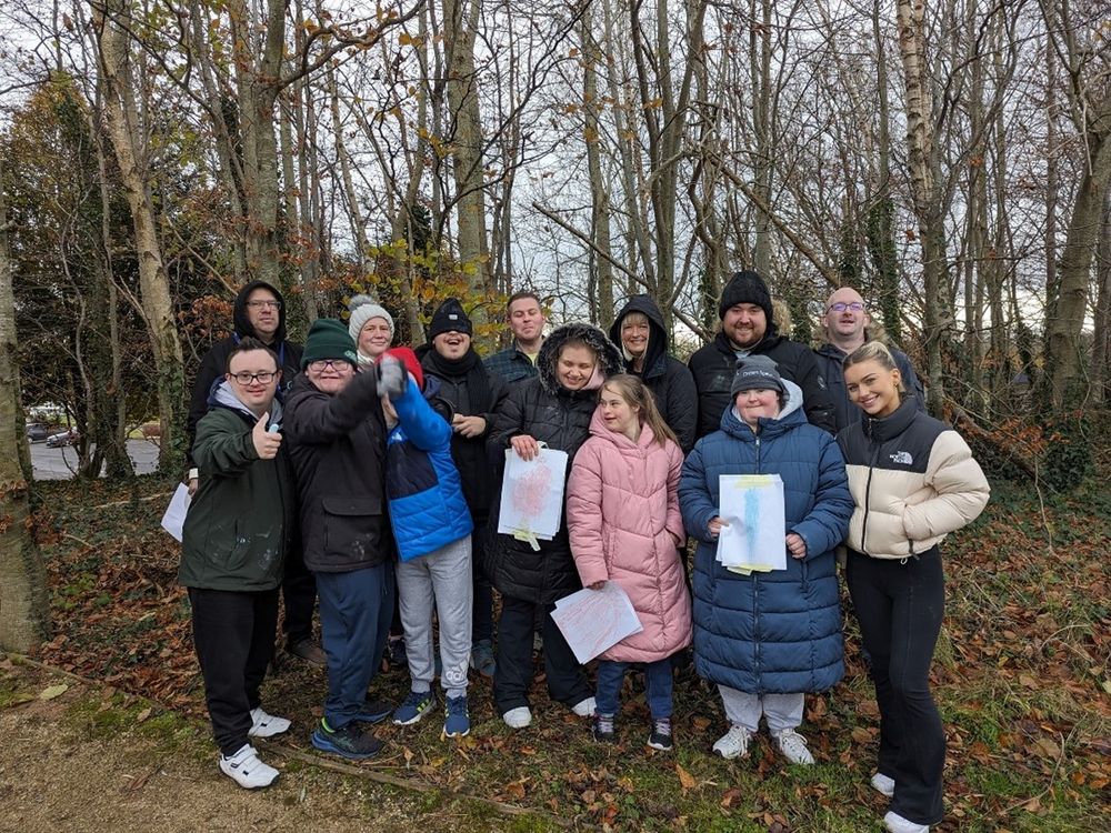 Group of 14 white female and male stand in wooded area smiling towards camera