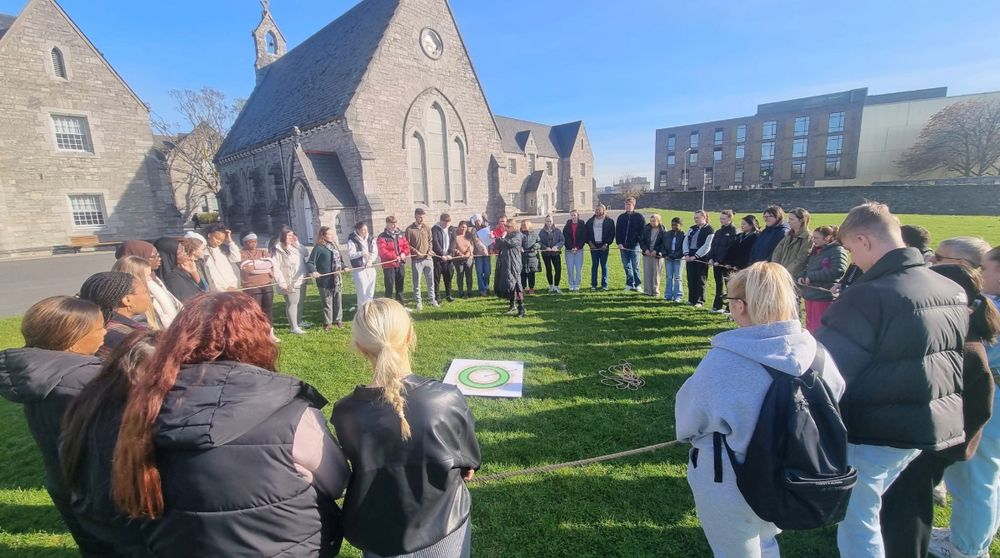 Group of people stand in circle outdoors with both hands on a rope for the stepping into the doughnut workshop