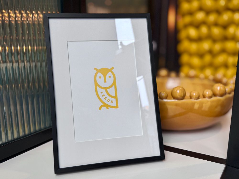 Gold printed owl on white paper in a black frame on a shelf.