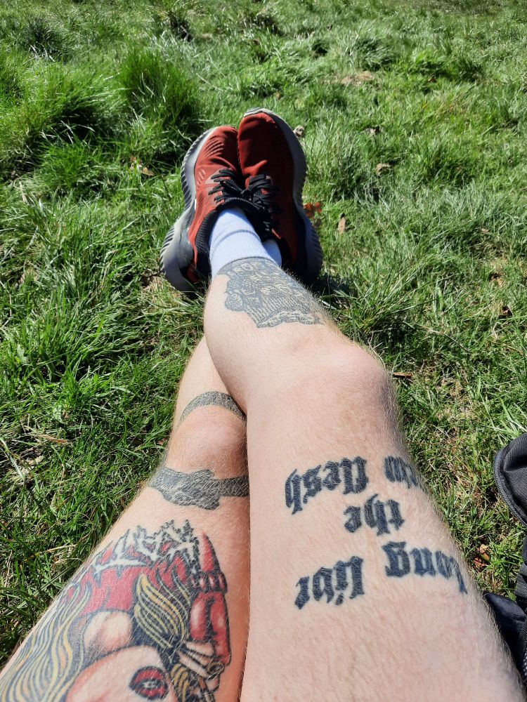 A pair of crossed tattooed legs lying on the grass 