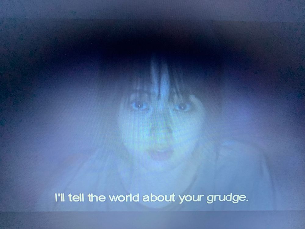 Close up of a woman’s face. Subtitle reads “I’ll tell the world about your grudge.”