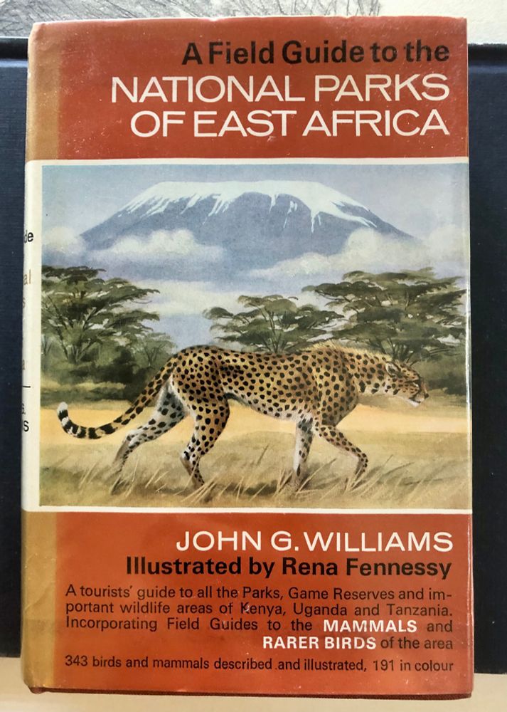 Cover of “A field guide to the national parks of east Africa” by John G. Williams, illustrated by Rena Fennessy — A tourists’ guide to all the Parks, Game Reserves and important wildlife areas of Kenya, Uganda and Tanzania. Incorporating field guides to the mammals and rarer birds of the area. 343 birds and mammals described and illustrated, 191 in colour. A terracota coloured dust-jacket with an illustration of a cheetah walking through a savanna grassland habitat with a mountain and trees in the background 