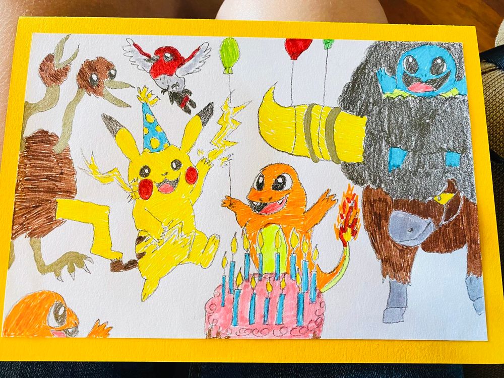 Hand-drawn birthday card on bright yellow background, featuring Pikachu in a blue and yellow-spotted pointy birthday hat, Charizard, Bouffalant, Squirtle, Dodrio and Fletching celebrating with balloons around a birthday cake with blue candles and pink frosting