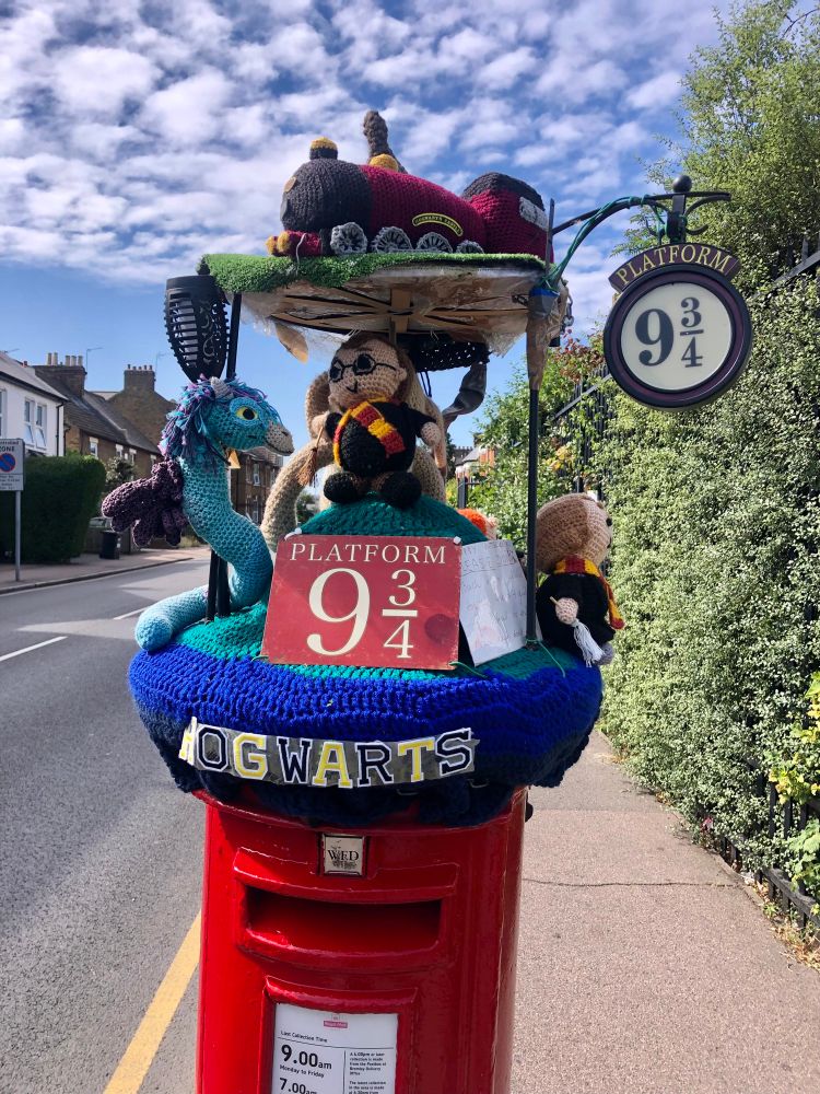Postbox with postbox topper showing characters from Harry Potter and the sign for platform 9 3/4 and steam train and some magical creatures