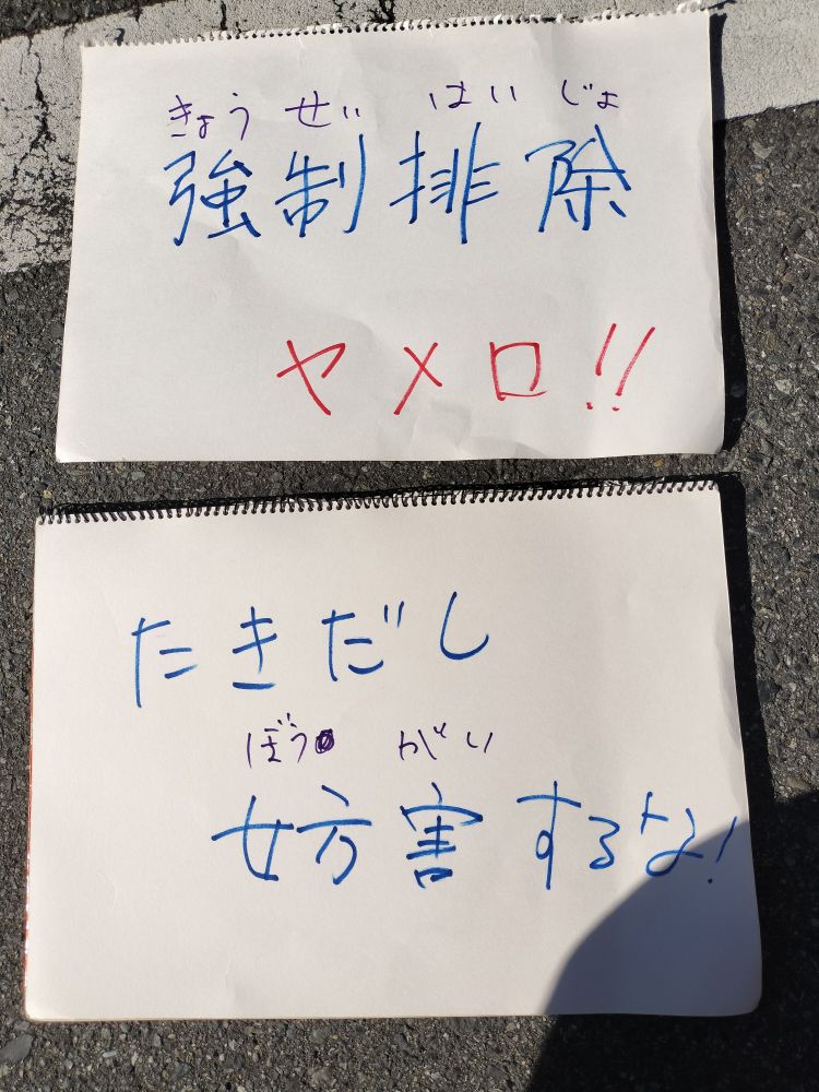 抗議のプラカード2枚。「強制排除　ヤメロ!!」と「たきだし　妨害するな!」と書かれている。