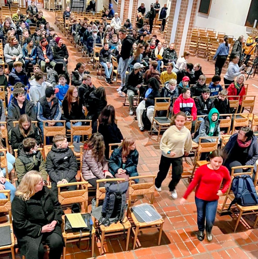 Kirchenraum, gut besetzt mit Jugendlichen, 2 Mädchen laufen durch den Mittelgang 