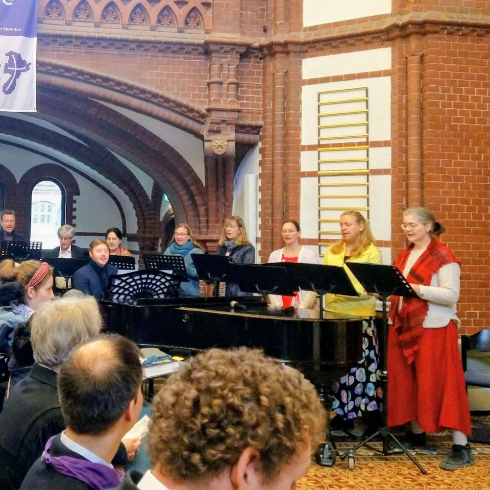 Chor singt, Mann spielt am Flügel in Backsteinkirche.