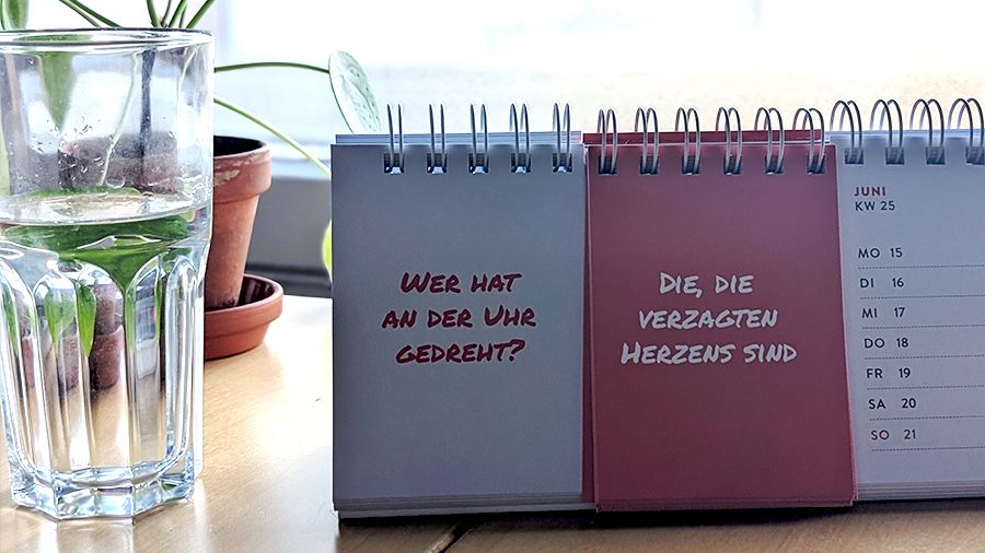 Klapp-Tischkalender "Wer hat an der Uhr gedreht?" "Die, die verzagten Herzens sind." neben Glas Wasser und Topfpflanze