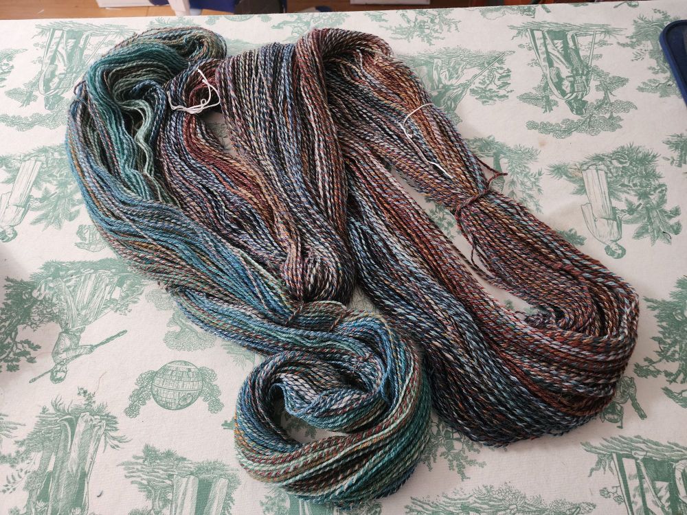 Photo of two skeins of homespun yarn. They're 3 ply sport weight in colors of teal, rust, blue, and white.