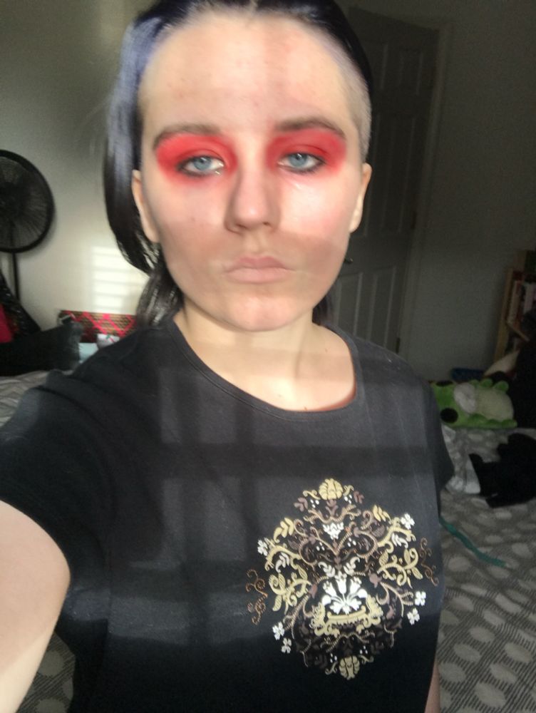 Dorian in red makeup, lighting makes them look like they have stubble