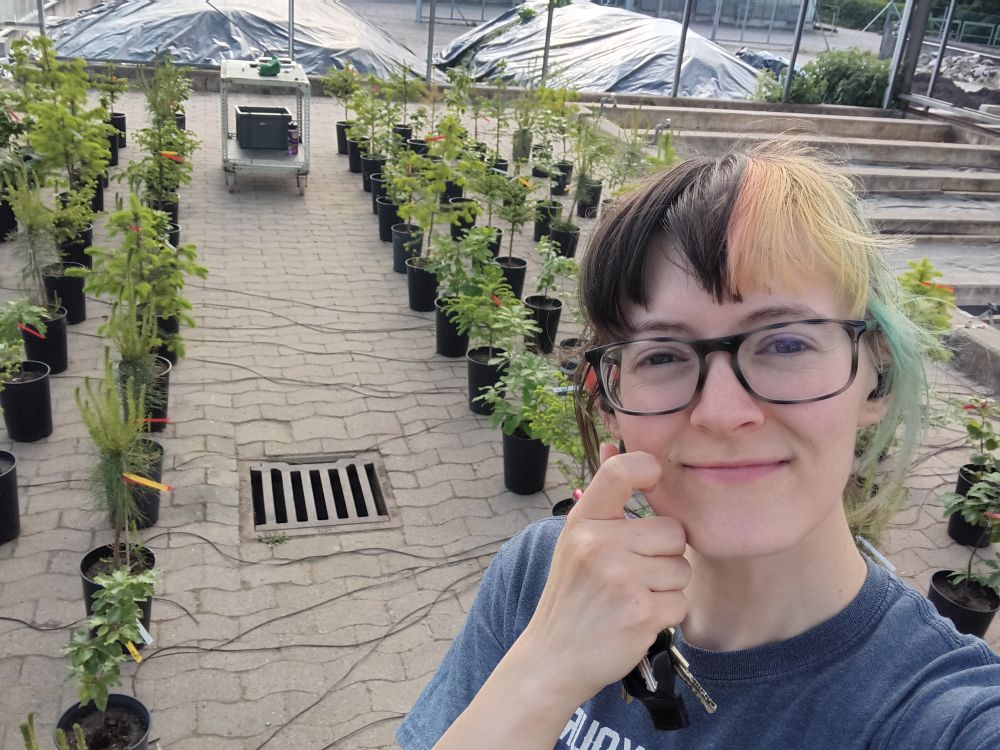 Myself smiling at the camera with a background of potted saplings.