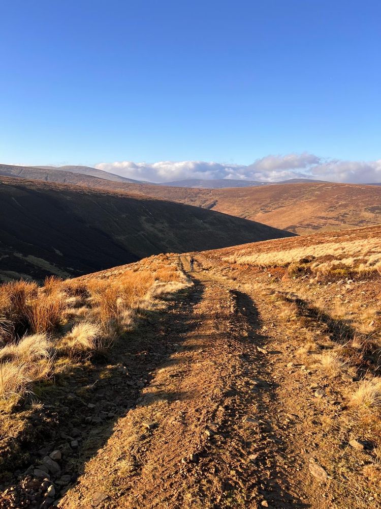 Distant cyclist on gravel incline with hills in the background. 