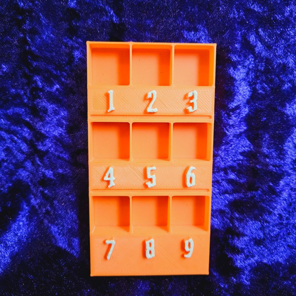 An orange rectangle with numbers 1-9 on it and a divot above each number for a dice to sit in