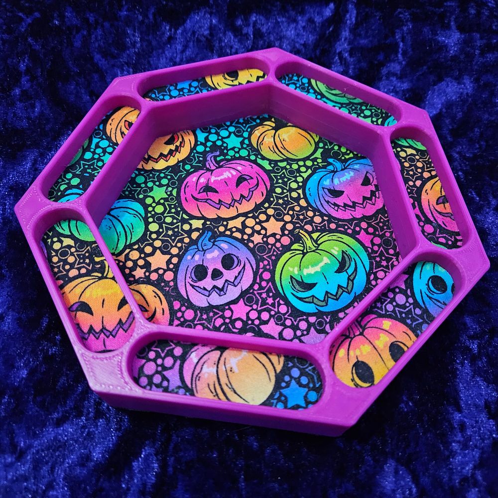 A 7 sided dice tray in magenta with pockets round the outside for dice and a rainbow pumpkin lining