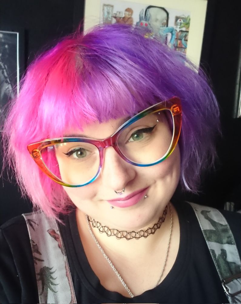 A person with pink and purple hair and large rainbow glasses smiling 