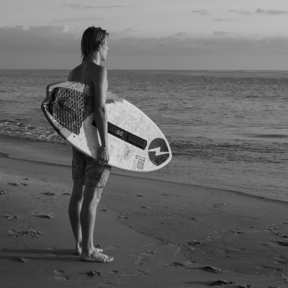 A surfer standing on a beach looking out over the water