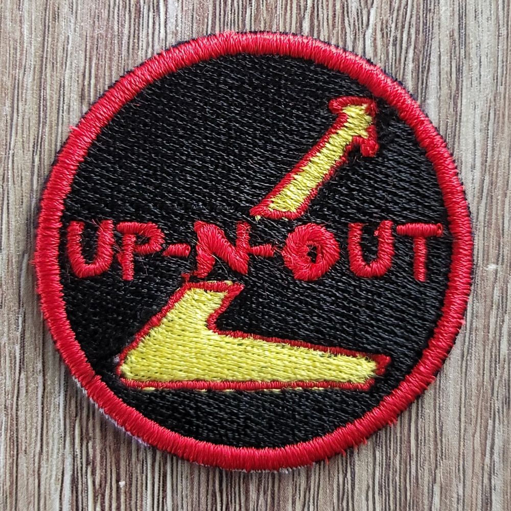 The Up-N-Out logo. The In-N-Out swoosh tilted upwards on a roundrel with UP-N-OUT in the center