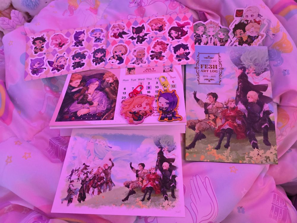 Various FE3H merchandise laid out on a bed