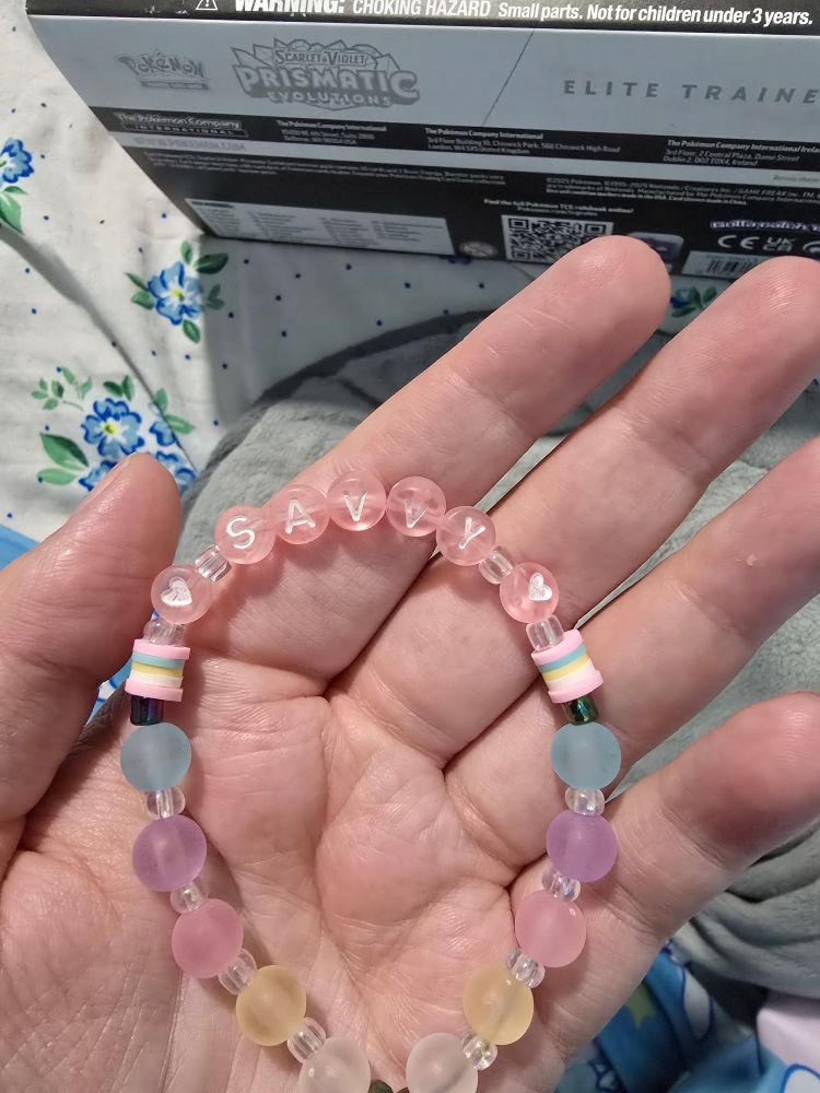 A friendship bracelet done in blue, pink, purple, yellow and white pastel beads, it says "💜Savvy💜" in pink beads