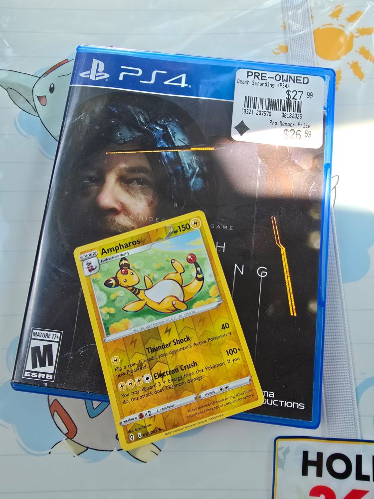 A picture of the case for the death stranding game, there is also an ampharos card on top of it. The game case and card are sitting on top of a card binder with togepi, togetic, and togekiss on it.