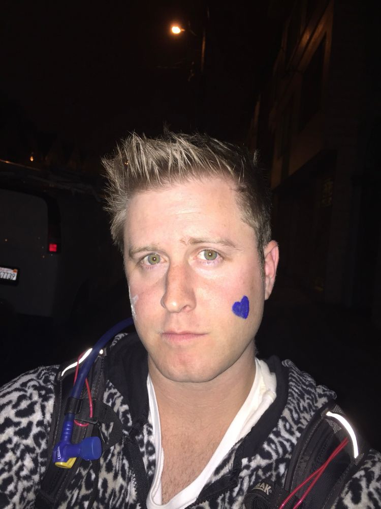 a sad looking emma with a blue face paint heart and a star on her other cheek. she's got short spiky blonde hair and she's, well, not smiling but doing a sad smirk? 

she's wearing a snow leopard onesie and a camelbak hydration pack. 