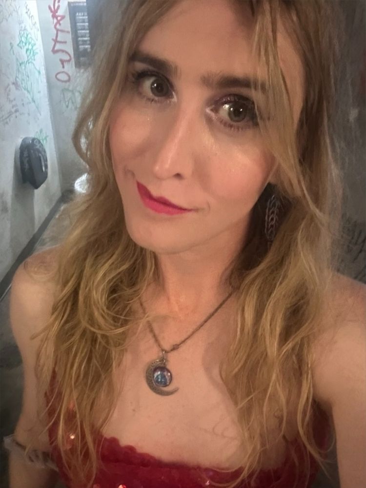 emma selfie from the bathroom at the rave wearing a red sequin dress that showed her entire ass and a cosmic crescent moon necklace. she's got blonde hair down her shoulders and a slight smile 