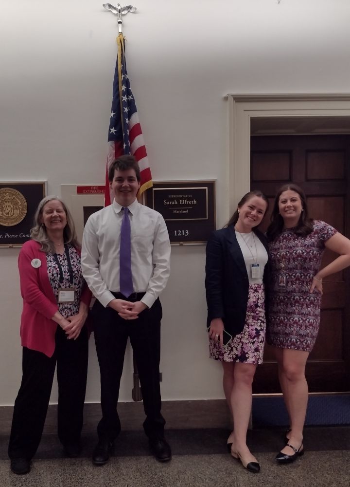 My nephew and I are standing in front of a US flag and Rep Sarah Elreth's nameplate along with two young women in a building's hallway.