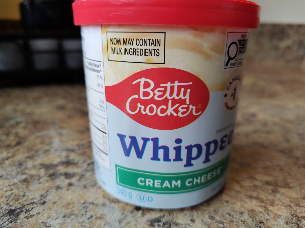 A tub of Betty Crocker cream cheese with the warning label "now may contain milk ingredients."