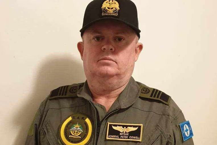fake admiral with a cap that still looks oversized on his gigantic head with a gaudy fake insignia. he has three more oversized patches on his jacket that are very poorly stuck on