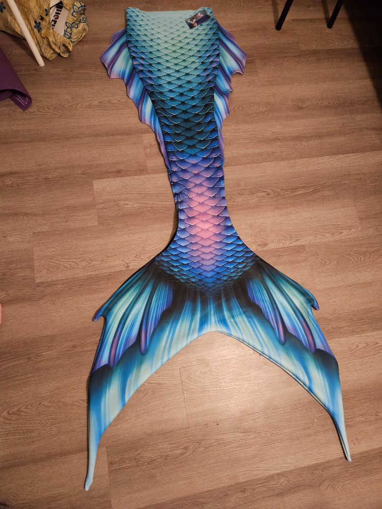 A Mertailor Out of the Sea tail laid out. It's in shades of blue, purple, and teal with highlights in a soft pink.